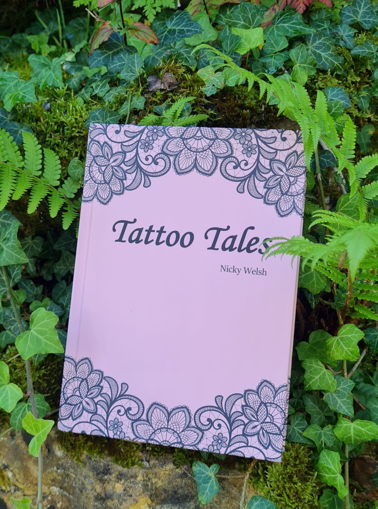 The pink “Tattoo Tales” book propped up among ivy leaves