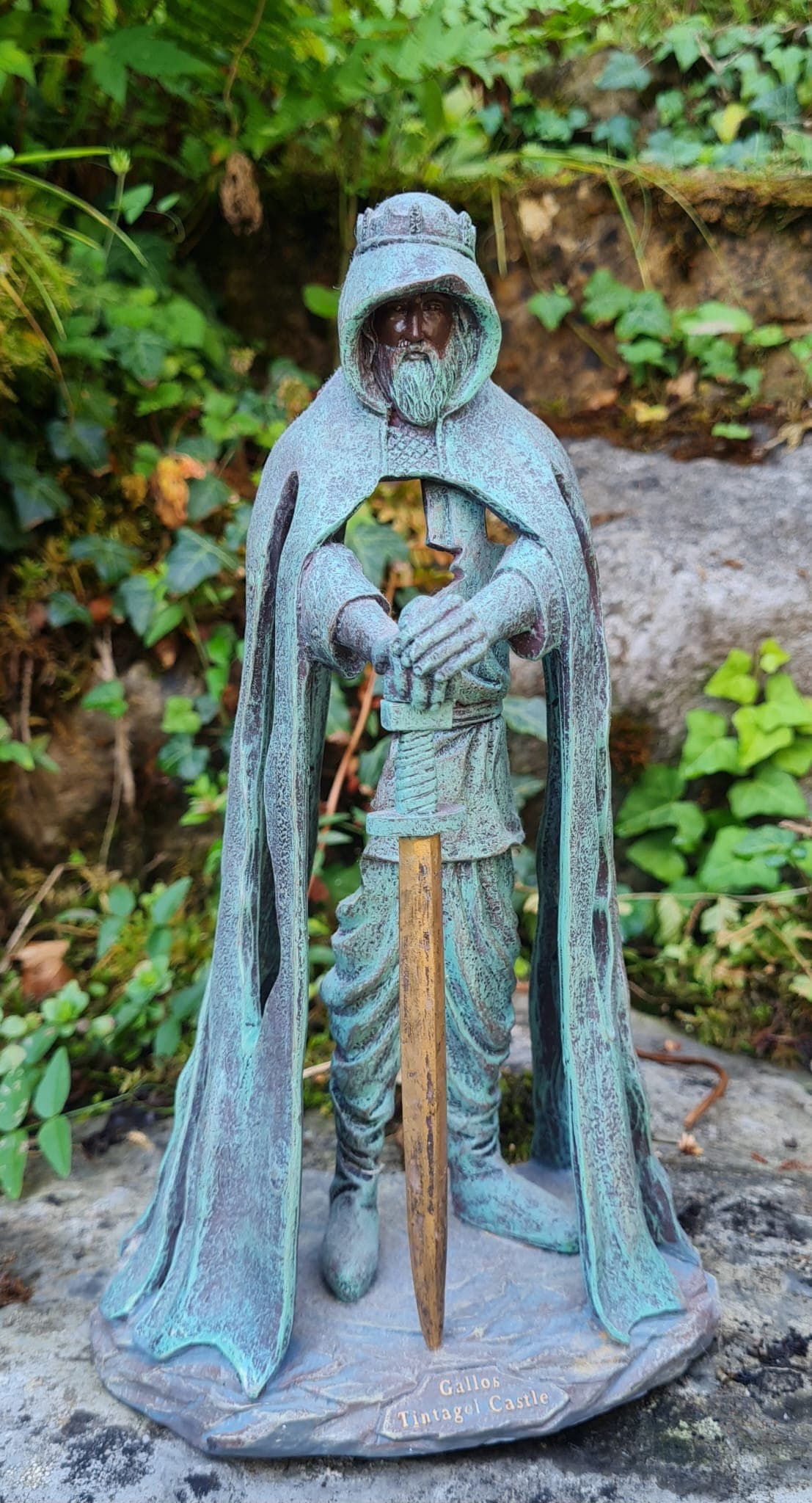 Weathered stone statue of a hooded figure in a green garden