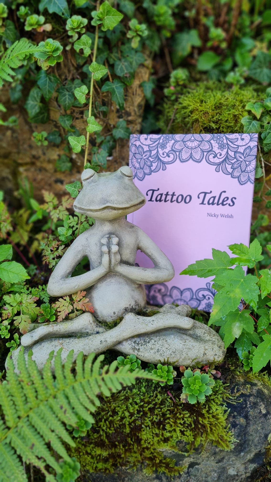 The book leaning against a stone frog among ferns