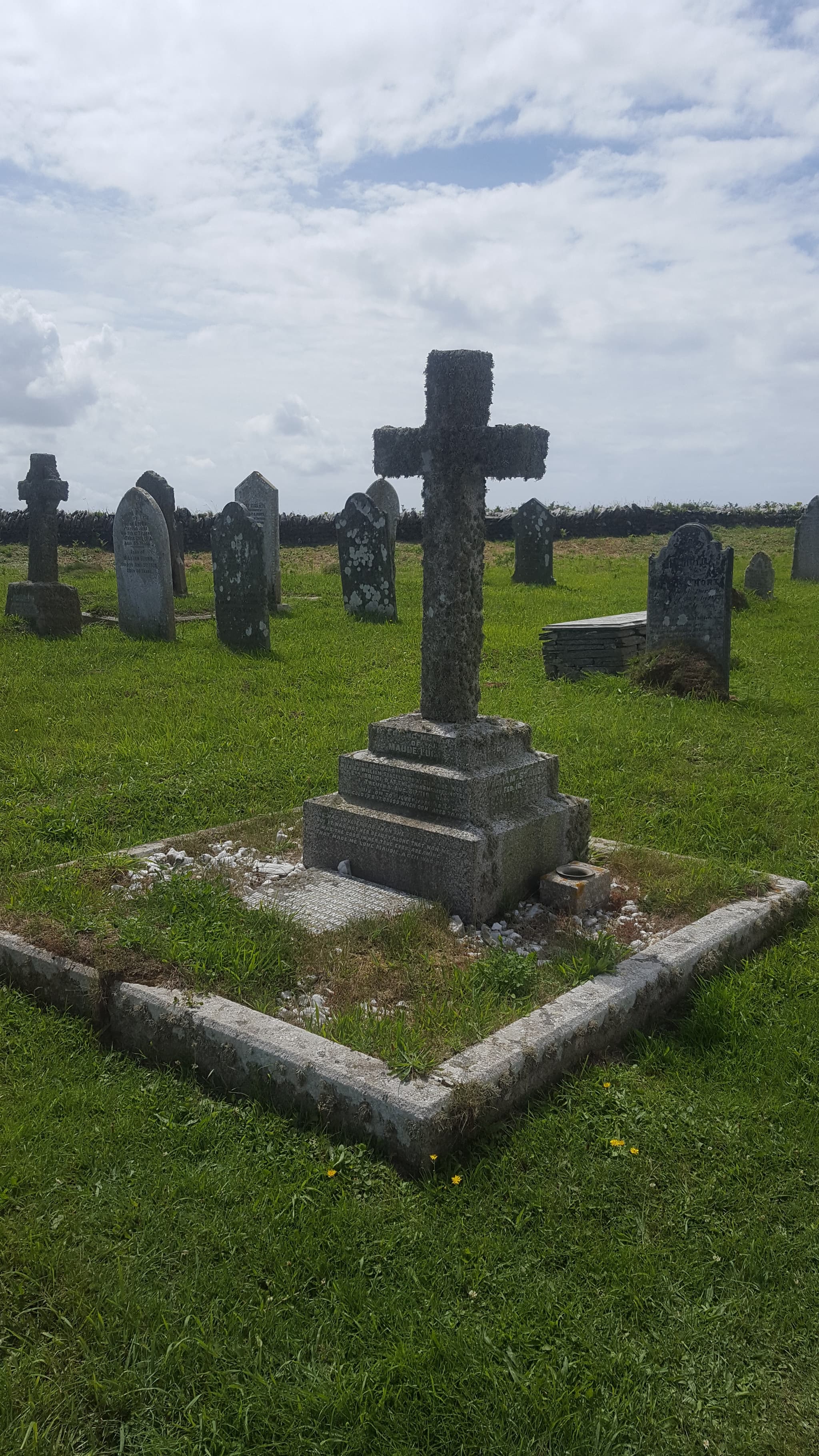 Ein verwittertes Steinkreuz zwischen Grabsteinen auf einem walisischen Friedhof