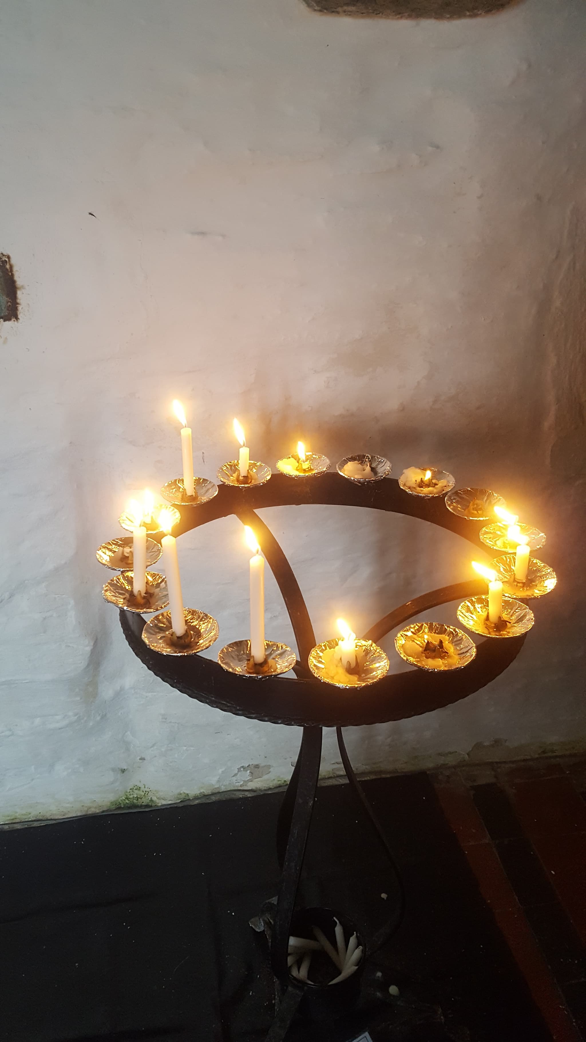 Brennende Kerzen auf einem schmiedeeisernen Ständer in einer dunklen walisischen Kirche